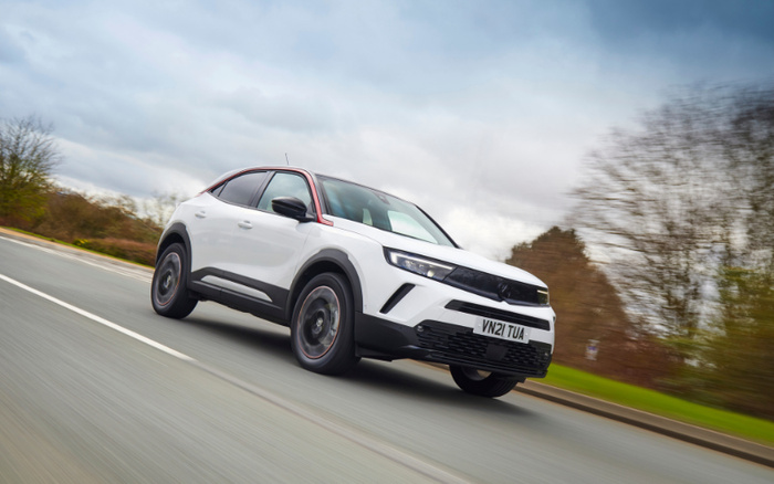 White and black modern SUV driving on a road with motion blur, registration plate VN21 TUA, under a cloudy sky with trees in the background, showcasing a new car model ideal for buyers interested in used cars and new cars.