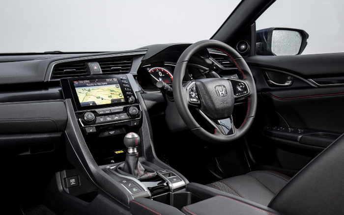 Interior view of a modern Honda car featuring a black leather steering wheel with Honda logo, digital dashboard, touchscreen navigation system displaying 'Ready to Navigate', manual gear shift lever with red stitching, black leather seats with red stitching details, and various control buttons on the centre console. Suitable for showcasing used cars and new cars.