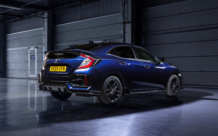 Rear side view of a dark blue Honda Civic hatchback car with UK license plate RX69 UYN, parked inside a large industrial garage with grey rolling shutter doors, showcasing a sleek design and black alloy wheels, suitable for advertising used cars and new cars.