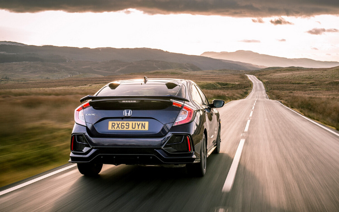 Rear view of a black Honda Civic car with registration plate RX69 UYN driving on a deserted road through rolling hills under a cloudy sky, representing used cars and new cars in a scenic countryside setting.