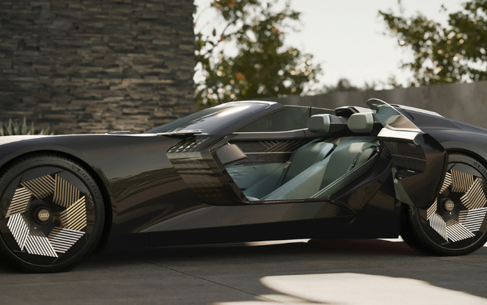 Sleek black Audi concept car with futuristic design featuring scissor doors open to reveal luxurious light grey and black interior seats, parked on a driveway with a stone wall and greenery in the background. The car showcases advanced wheel design with intricate geometric patterns and the Audi logo at the centre, representing the innovation in both used cars and new cars markets.