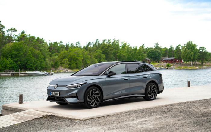 Modern grey Volkswagen electric car parked on a waterfront concrete pier with a backdrop of green trees and houses across the water, showcasing a sleek design ideal for buyers interested in used cars or new cars.
