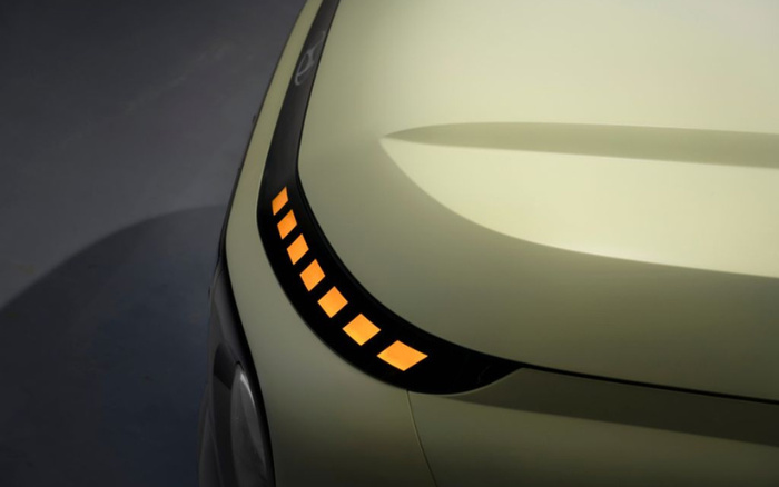 Close-up of the front left corner of a modern car in a pale yellow colour, showcasing a sleek, curved LED daytime running light with illuminated orange rectangular segments, highlighting the vehicle's futuristic design, relevant for used cars and new cars.