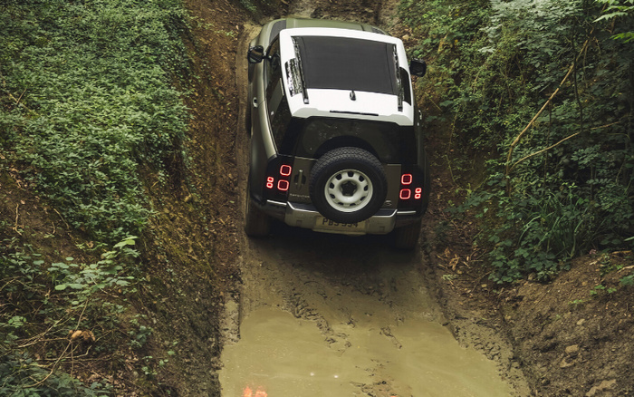 Rear view of a 4x4 SUV driving uphill on a narrow muddy trail surrounded by dense green foliage and uneven terrain, showcasing off-road capabilities relevant to new cars and used cars suitable for rugged outdoor adventures.