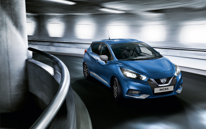 Blue Nissan Micra car driving inside a modern concrete parking garage with motion blur, showcasing the front and side view of the vehicle. The licence plate reads 'MICRA'. This image highlights both used cars and new cars options available.