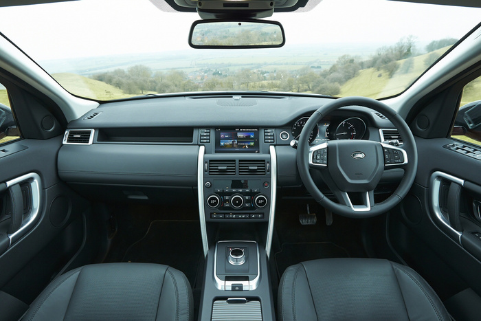 Interior view of a modern Land Rover vehicle with a steering wheel featuring Land Rover logo, digital dashboard, central control panel with climate control settings displaying temperatures of 22.0°C, and multimedia screen showing radio 1, climate outside 9°C, and various control options. The image highlights the steering on the right side, leather seats, and a scenic countryside view through the windshield, representing features of used cars and new cars.