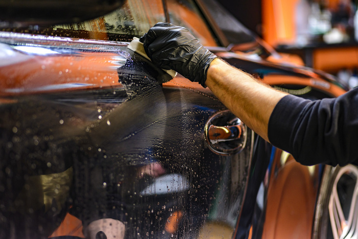 Close-up of a person wearing a black glove cleaning the wet surface of a black car with a cloth in a garage or workshop, highlighting careful detailing work often needed for maintaining used cars and new cars in pristine condition.