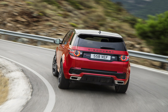 Red Land Rover Discovery Sport with registration plate 558 VEF driving on a curved mountain road with guardrails and blurred natural rocky and green surroundings, showcasing a new car model suitable for promotional use in used cars and new cars sales.