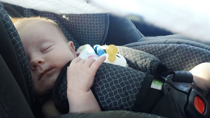 Sleeping baby secured in a patterned black and grey car seat with a yellow pacifier clipped to the harness, highlighting the importance of child safety in used cars and new cars.