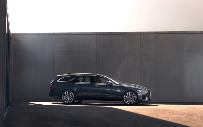 Sleek dark grey Jaguar XF Sportbrake parked sideways against a modern grey concrete wall under soft sunlight, showcasing the luxury estate car's streamlined design, alloy wheels, and tinted windows, ideal for both used cars and new cars enthusiasts searching for sophisticated vehicles.