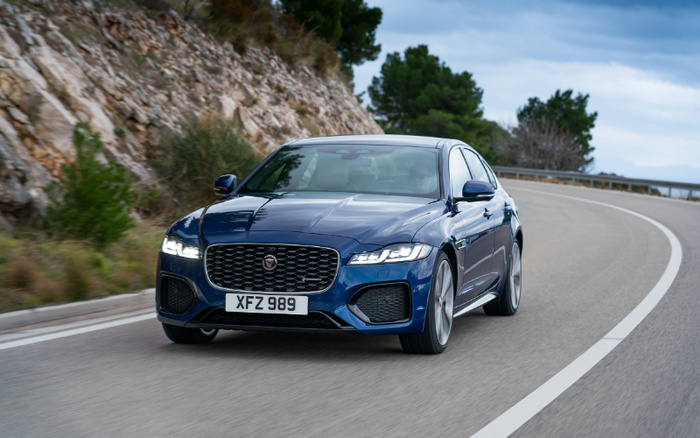 Blue Jaguar XF luxury car with license plate XFZ 989 driving on a curved mountain road, surrounded by rocky cliffs and trees, showcasing a sleek modern design, suitable for used cars and new cars buyers.