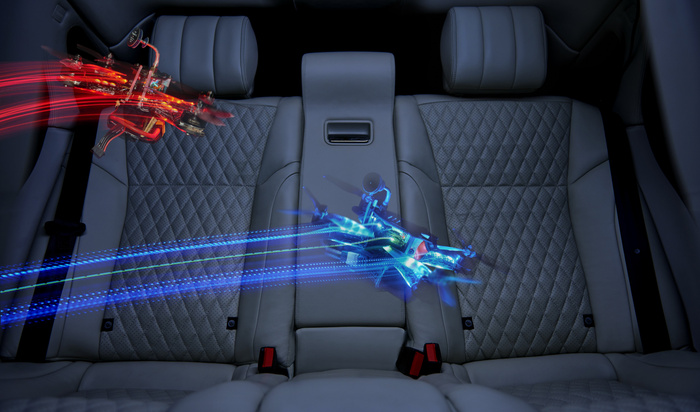 Interior of a luxury car with quilted dark grey leather seats and centre armrest, featuring two small racing drones flying above the rear seats leaving red and blue light trails, representing speed and technology in used cars and new cars.