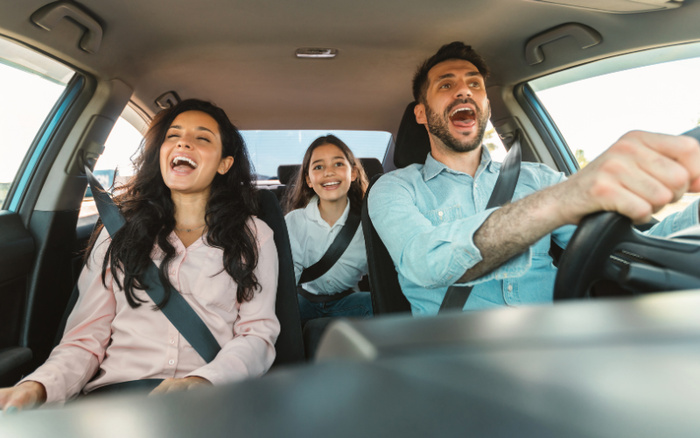 Happy family of three enjoying a car ride together, with the father driving, the mother sitting in the front passenger seat, and their daughter seated in the back, all wearing seat belts in a clean, modern vehicle. Perfect representation for used cars or new cars promoting joyful family travel experiences.