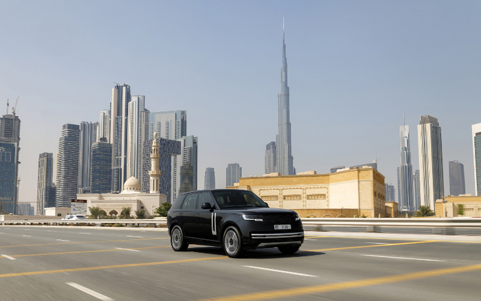 A black luxury SUV driving on a wide road in Dubai with the Burj Khalifa and modern skyscrapers in the background. The image represents the cityscape of Dubai and a high-end vehicle suitable for new cars or used cars markets.