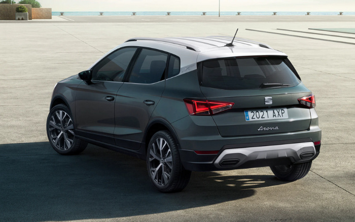 Rear and side view of a dark grey SEAT Arona compact SUV with a white roof, parked on a concrete surface by the sea. The car features sharp, modern taillights and a European license plate reading '2021 AXP'. This image is ideal for showcasing used cars or new cars in a coastal or urban environment.