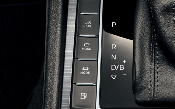 Close-up view of a car's gear shift panel and driving mode buttons, showing labels for SPORT, e MODE, and MODE with a car icon, alongside a fuel button. The gear shift indicators include P, R, N, D/B with plus and minus signs, and a down arrow. The image captures details of the car interior, highlighting controls typically found in used cars and new cars.