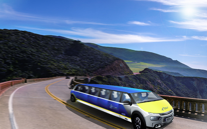 Blue and yellow customised limousine driving on a winding coastal road with mountainous landscape and clear blue sky in the background, representing luxury vehicles including used cars and new cars.