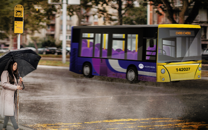 A woman holding a black umbrella stands at a bus stop on a rainy day. The yellow bus stop sign shows bus numbers 6 and 13. A purple and yellow bus with the registration number 142027 and the name 'Northern' on its side is approaching, with destination sign displaying 'CHOO CHOO'. The street and surroundings appear wet, indicating recent rain. This image contrasts public transportation with options for used cars and new cars for travel.