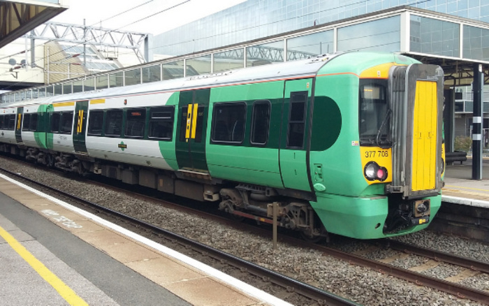 Green and white electric passenger train numbered 377 708 at a modern train station platform, featuring a distinct yellow front panel, with overhead electrical wires and a large glass building in the background. This image does not contain any text or references to used cars or new cars.