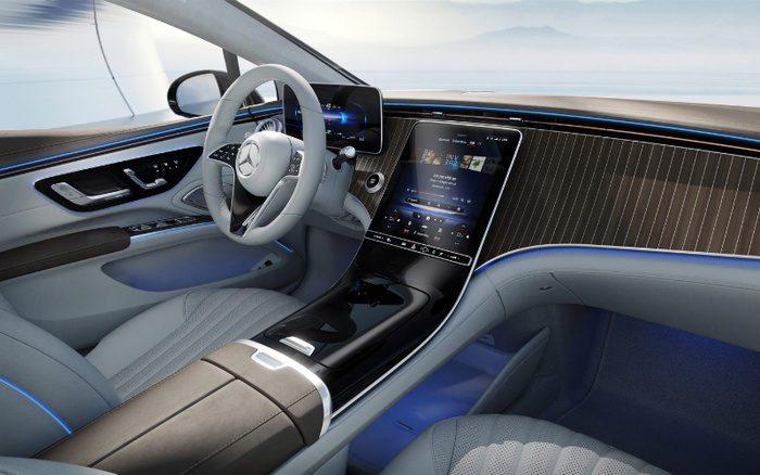 Interior view of a new Mercedes-Benz car showcasing a modern, luxurious dashboard with a large vertical touchscreen display, digital instrument cluster, leather steering wheel with Mercedes logo, ambient blue lighting, wood panel trim, and premium light grey leather seats, highlighting advanced technology and comfort features ideal for new cars and used cars shoppers.