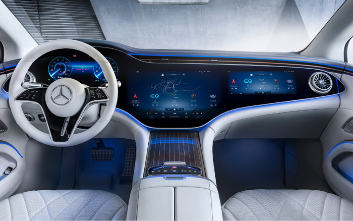 Interior view of a new Mercedes-Benz electric car featuring a white steering wheel with the Mercedes logo, dual widescreen digital displays showing navigation, media, and vehicle settings including EQ mode, surrounded by ambient blue lighting and quilted white leather seats, showcasing modern technology and luxury design ideal for used cars or new cars buyers.