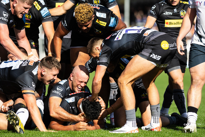 Rugby players in black and white kits engaged in a match on green grass, with visible sponsor logos including Bradford, carparis, Vertu, and Troy on their uniforms, capturing intense physical action and teamwork during the game, unrelated to used cars or new cars.
