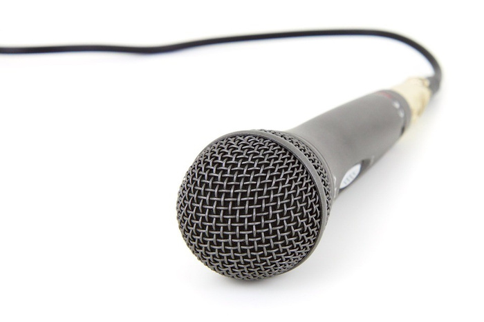 Close-up of a wired microphone with a black mesh grille and black body on a white background. No text related to used cars or new cars is visible on the microphone.