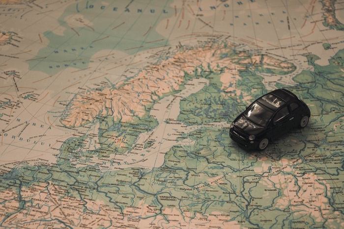 Black toy car placed on a detailed vintage map showing Northern Europe, including countries such as Sweden, Norway, Finland, Denmark, Poland, and parts of Russia and the Baltic states, displaying cities like Stockholm, Helsinki, and Warsaw. The image symbolises travel or navigation, related to used cars and new cars.