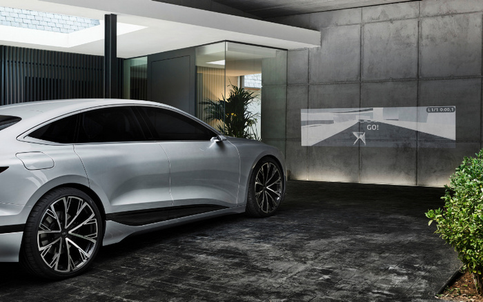 Silver electric car parked in a modern driveway with large black and silver wheels, sleek design, and tinted windows. The background shows a contemporary house with glass walls and plants. A digital projection on the concrete wall displays a driving simulation with the word 'GO!' and directional arrows, suggesting advanced technology integration. Ideal image for used cars and new cars showcasing innovation and style.