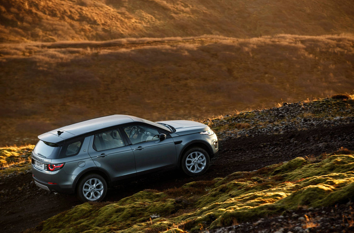 Silver Land Rover Discovery SUV driving off-road on a rugged dirt path with mossy ground and hills in the background during golden hour, showcasing a modern new car ideal for adventurous terrain, highlighting features suitable for buyers of used cars and new cars.