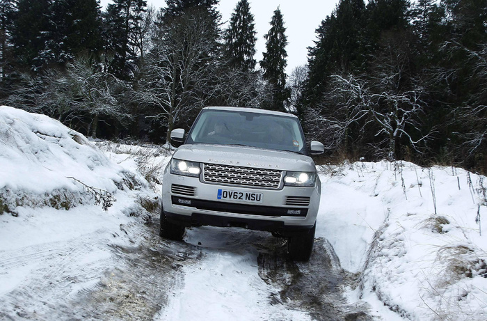 Silver Range Rover vehicle driving on a snowy off-road path surrounded by snow-covered trees. The car's headlights are on and the front license plate reads 'OV62 NSU'. This image showcases a durable SUV suitable for winter conditions, ideal for buyers interested in used cars or new cars with off-road capability.