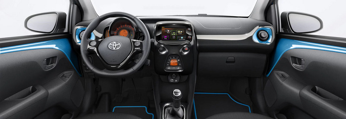 Interior of a Toyota car showing the steering wheel with Toyota logo, dashboard with orange illuminated speedometer and digital display, central touchscreen interface displaying menu options including phone, connect, setup, audio source, and car information, temperature control set at 20°C, manual gear stick, black and blue trim door panels, and side mirrors visible through windows, representing the stylish and modern features of used cars and new cars.