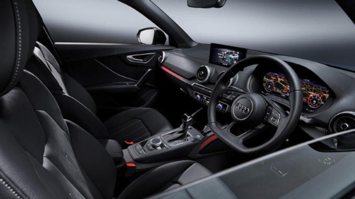 Interior view of a modern Audi car showing the driver's seat, steering wheel with Audi logo, digital dashboard displaying navigation and vehicle information, centre console with gear shift and control buttons, and infotainment screen. The sleek black leather seats and red accent lighting highlight the car's premium design, suitable for buyers interested in used cars or new cars.