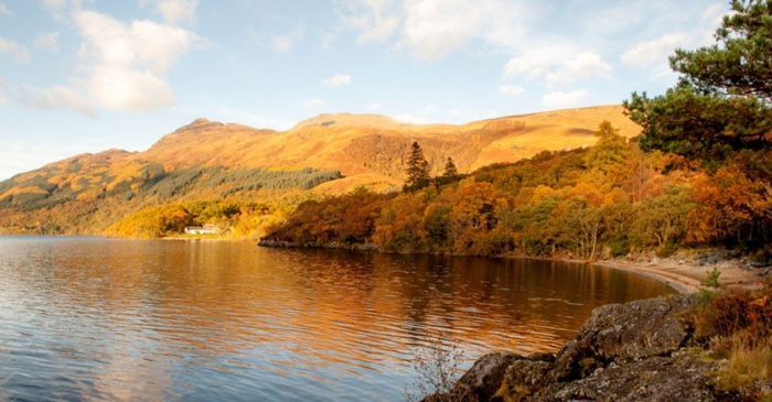 Scenic view of a calm lake surrounded by autumnal trees and hills bathed in golden sunlight, with no visible text or references to used cars or new cars.