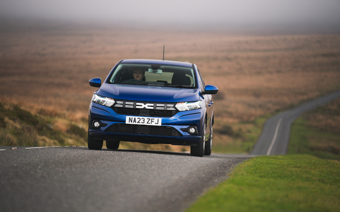 Blue Dacia Sandero car with license plate NA23 ZFJ driving on a rural road with grassy and moorland surroundings, viewed from the front, suitable for advertising used cars and new cars.