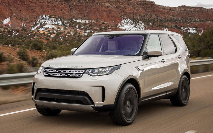 White Land Rover Discovery SUV driving on a road with rocky and tree-covered landscape in the background, showcasing a new car model ideal for used cars and new cars buyers.
