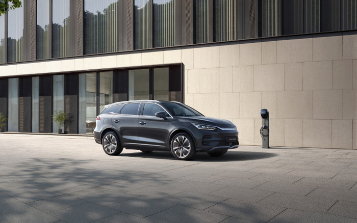 New sleek grey electric SUV parked outside a modern building next to a vehicle charging station, showcasing a clean and futuristic design suitable for used cars and new cars buyers.