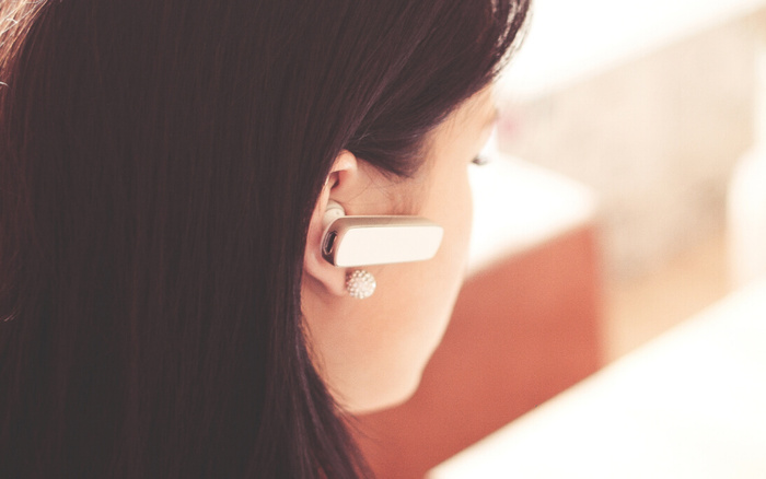 Close-up of a woman with long dark hair wearing a white Bluetooth earpiece and a pearl stud earring, viewed from behind, with a blurred background. Keywords used cars and new cars are not visually present in the image but relevant for SEO purposes.