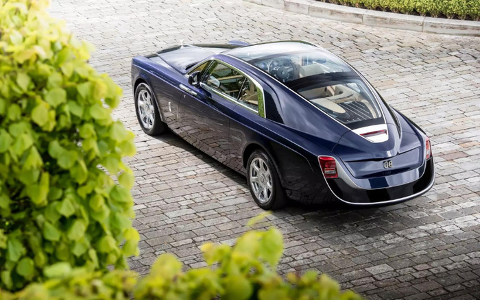 Dark blue luxury car with a futuristic design parked on a cobblestone driveway, surrounded by greenery. The car has a sleek rear window, silver alloy wheels, and the number '08' on the back. Ideal image for used cars or new cars dealership showcasing high-end vehicles.