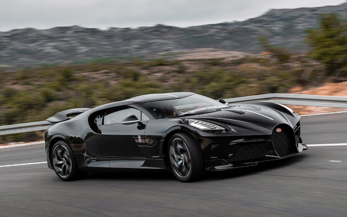 Black Bugatti supercar driving on a winding road with mountainous landscape in the background, showcasing a sleek and aerodynamic design, ideal image for used cars and new cars promotion.