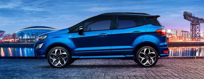 Side view of a blue compact SUV parked on a cobblestone surface by a waterfront at dusk with modern buildings and a crane in the background, showcasing a sleek design suitable for buyers looking for used cars or new cars.