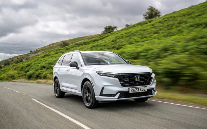 White Honda SUV with UK registration plate RA23 EGE driving on a countryside road with green hills and cloudy sky in the background, showcasing a modern new car model suitable for used cars and new cars market.
