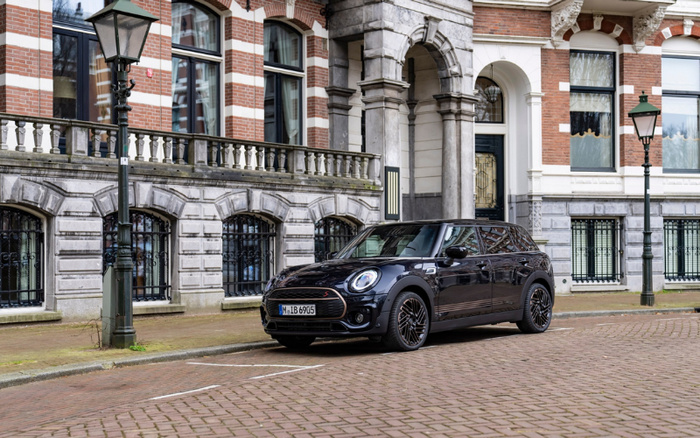 Black Mini Clubman parked on a cobblestone street in front of a classic European building with red brick and stone detailing. The car has a German license plate reading M LB 6905. Vintage street lamps are visible nearby. The image captures a used car in an urban setting, suitable for illustrating content about used cars and new cars.