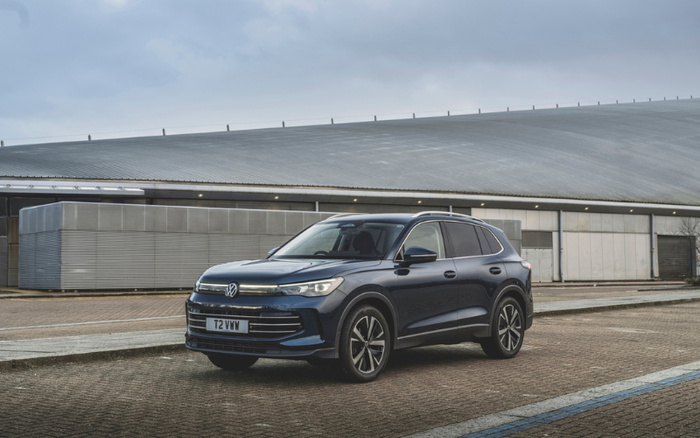 Dark blue Volkswagen SUV parked on a paved lot in front of a large industrial building under a cloudy sky. The vehicle has a front license plate reading T2 VWM. The image highlights a modern new car model suitable for buyers interested in used cars and new cars.