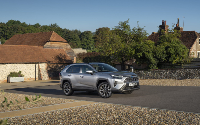 Silver Toyota RAV4 SUV with registration plate GP23 KUN parked on a driveway in front of a traditional stone and brick house with a brown tiled roof, surrounded by gravel and greenery, showcasing a new car model ideal for buyers looking for used cars and new cars options.