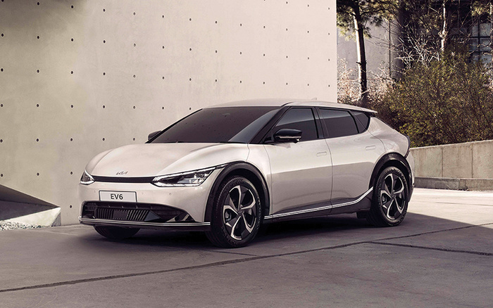 Silver Kia EV6 electric car parked beside a modern concrete wall under daylight, showcasing sleek design and aerodynamic curves, representing a new car model ideal for customers looking for new cars or used cars.