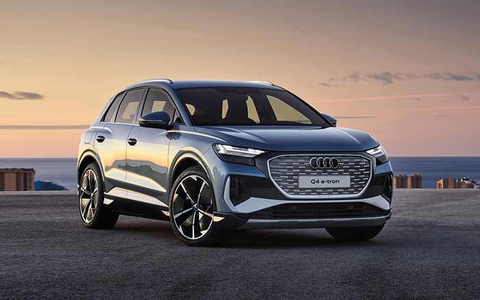 Audi Q4 e-tron grey electric SUV parked on rooftop at sunset with city and sea in background, showcasing sleek modern design, ideal for buyers searching for used cars or new cars.