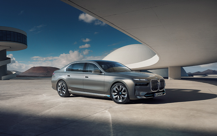 Silver luxury sedan parked in a modern, architectural outdoor setting under a curved concrete structure with clear blue sky and mountains in the background, showcasing a high-end new car ideal for buyers looking for quality used cars or new cars.