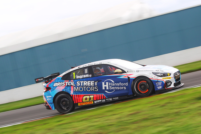 Race car with ‘Bristol Street Motors’ and ‘Hansford Sensors’ logos in blue, white, and red livery, number 01 on the side and driver name Ingram, speeding on a racetrack with visible brake disc glowing red. Sponsors on the car include Autocar, Scorpion, Purple Doc, CSG, Rocket, Global Sports, Third Millennium, Goodyear, and S2M.