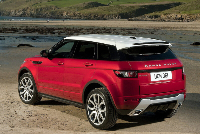 Red Range Rover Evoque with white roof parked on a sandy beach with cliffs and people in the background, UK license plate UCN 361, showcasing a stylish used or new car option.